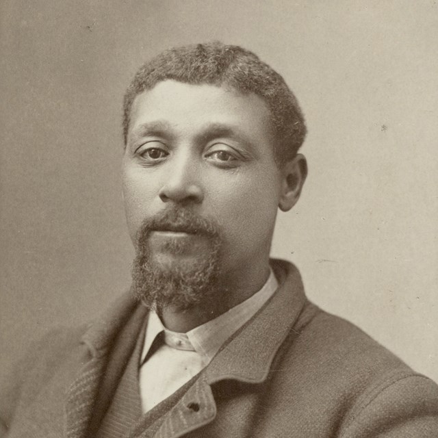 A Black man poses for a portrait wearing a suit