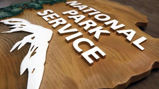 A wooden sign lying on a flat surface that reads "National Park Service" in white letters