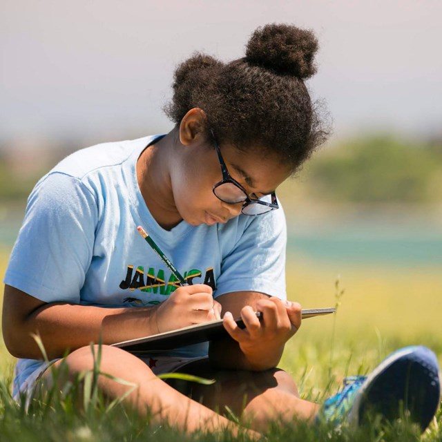 Girl sits in a field writing on her tablet