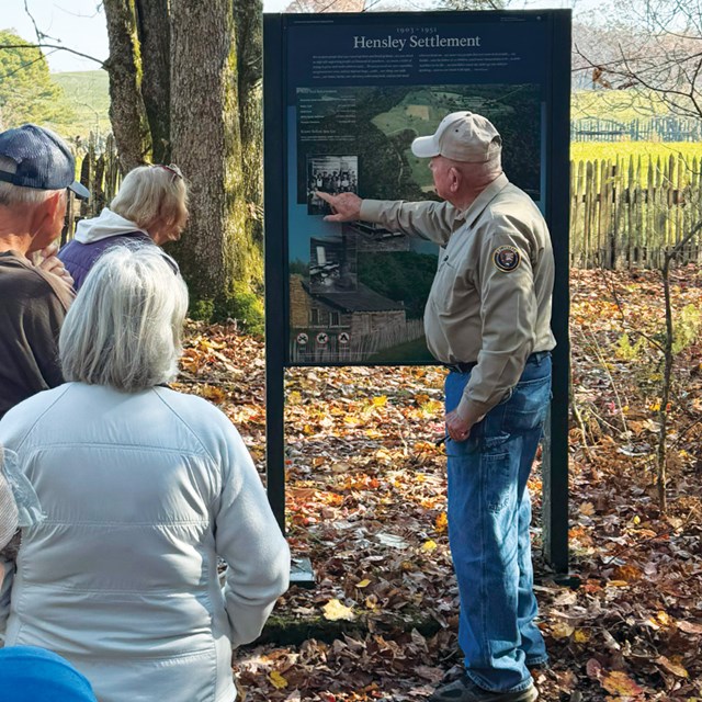 Volunteer giving a tour and talking in front of a wayside sign. 
