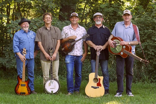 Five men of various ages stand in a row outdoors facing the camera with smiles. Each man carries a stringed instrument.