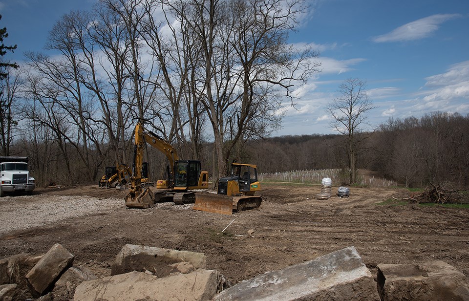 Large sandstone blocks and wooden beams lay scattered by a dumpster, shed, and barn.