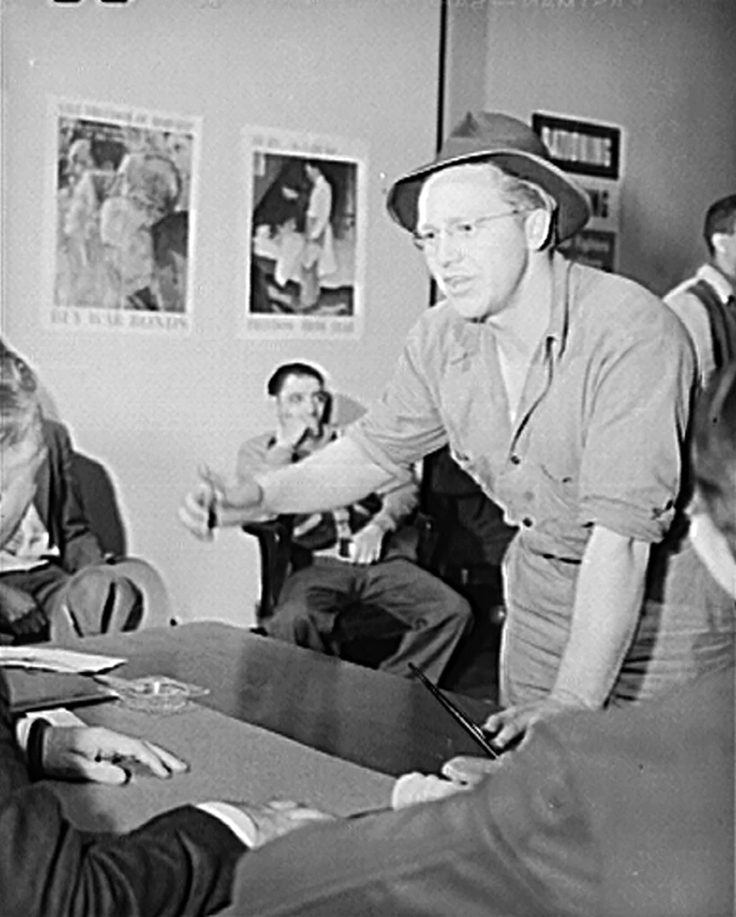 Stylized color image of a man in a suit, tie, and jaunty hat driving a convertible. In the passenger seat is a ghostly outline of Hitler.