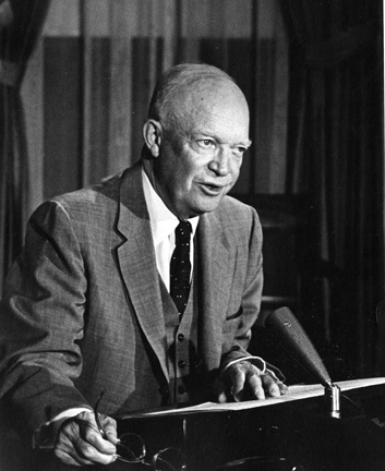 A man in a suit seated behind a desk and microphone