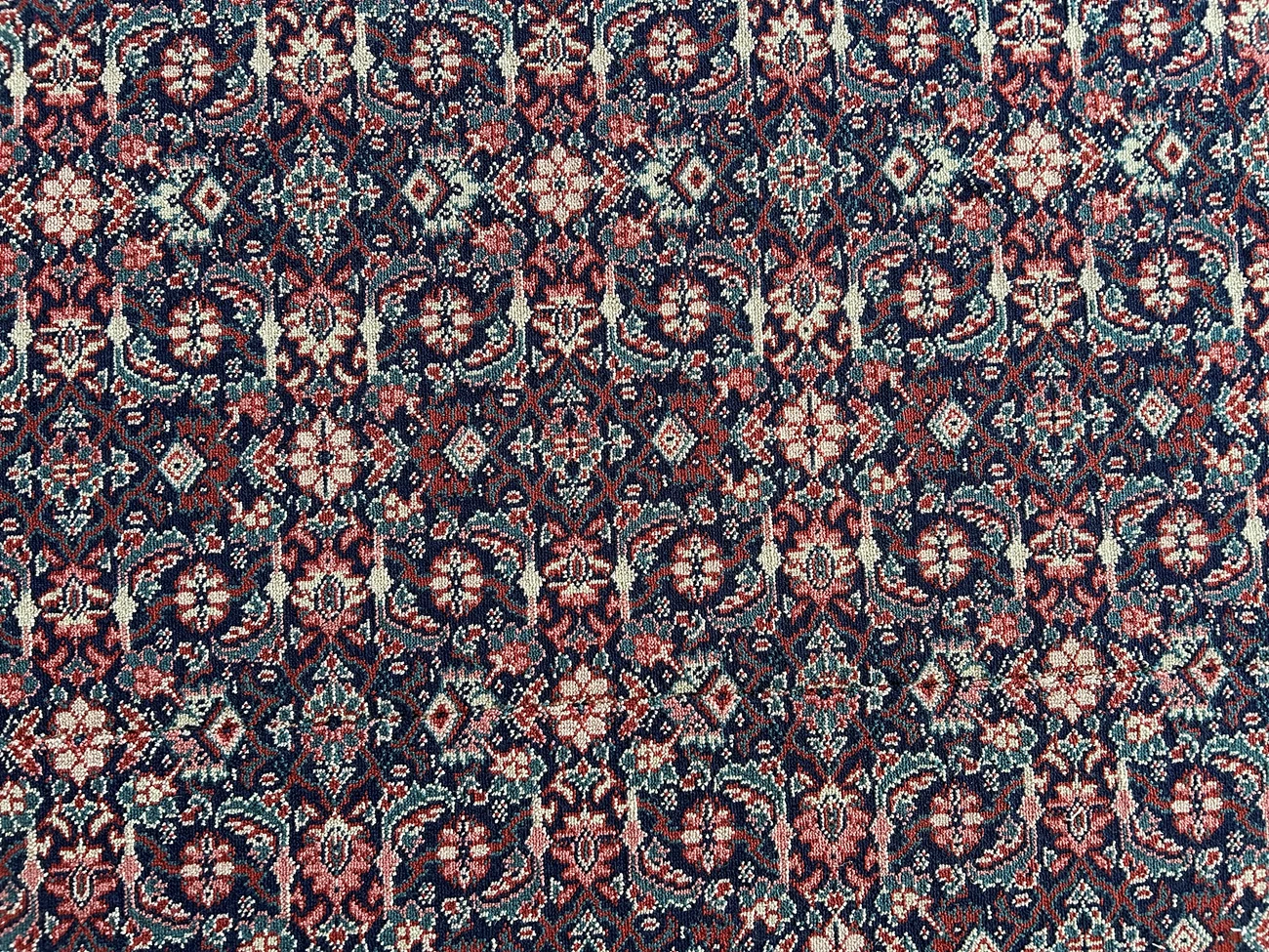 A close up of carpet with a green background and small repeating red pattern. The carpet is rippled due to water damage.