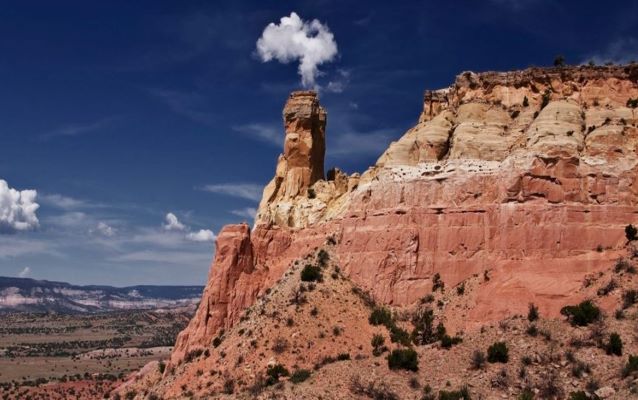 Sedimentary rock outcrop with greenery in the background and blue sky with clouds.