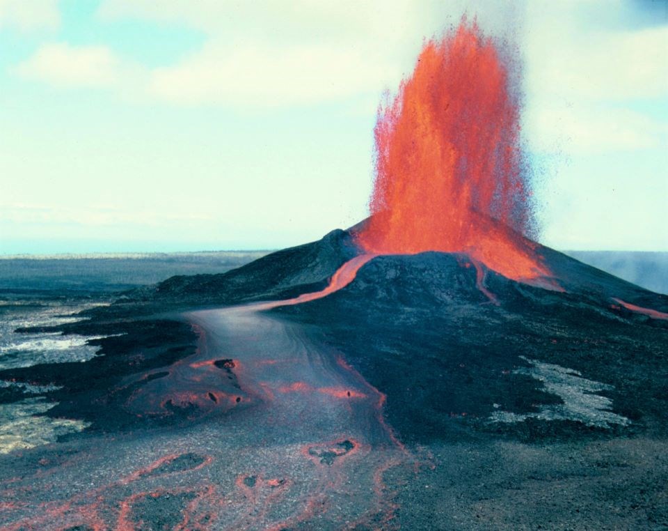 a dark cinder cone and lava field dotted with green plants