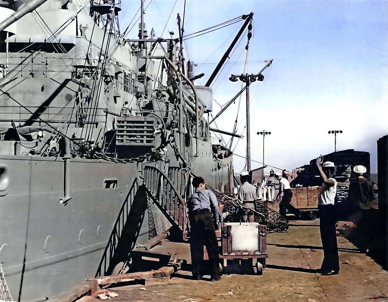 Four African American sailors are seen loading munitions onto a large ship.