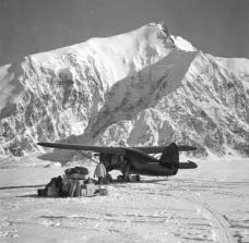 a plan on skis parked on a snowy field near a craggy white mountain