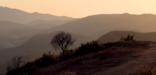 Mountain ridges recede into the distance while a lone hiker stands silhouetted on a trail at sunset