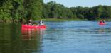 Canoeists paddle by tree lined shores