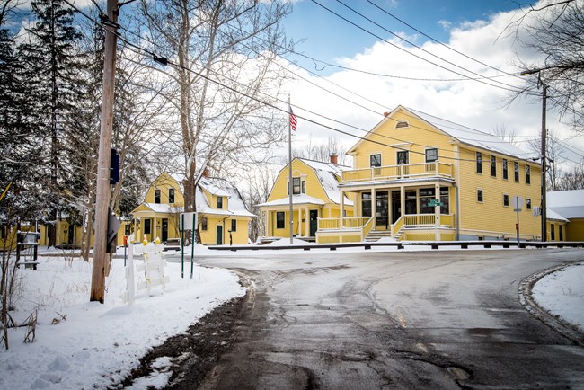 A row of yellow cottages at a road intersection, with snow on the ground.