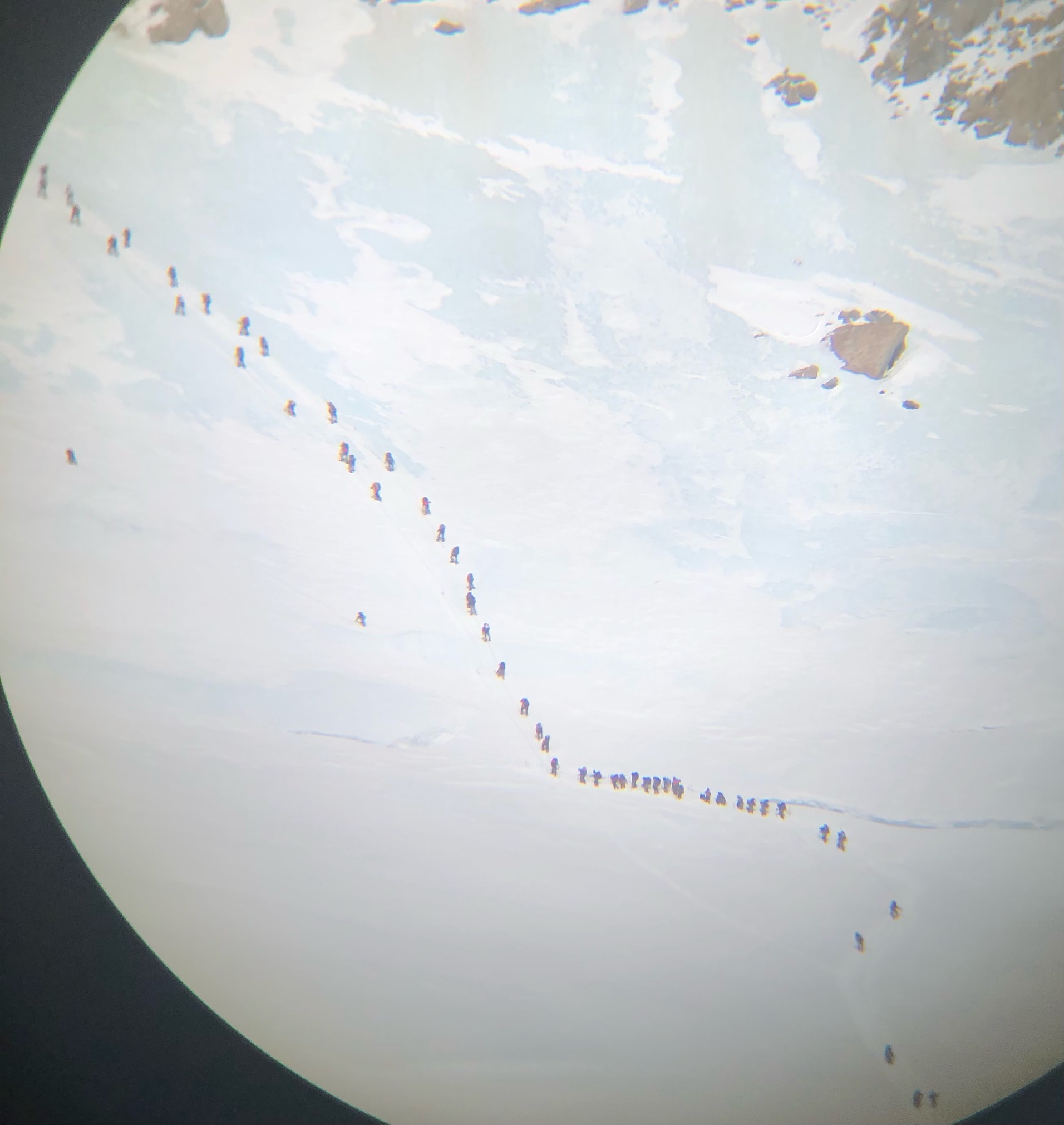 A long string of climbers wait in line to ascend a rope line