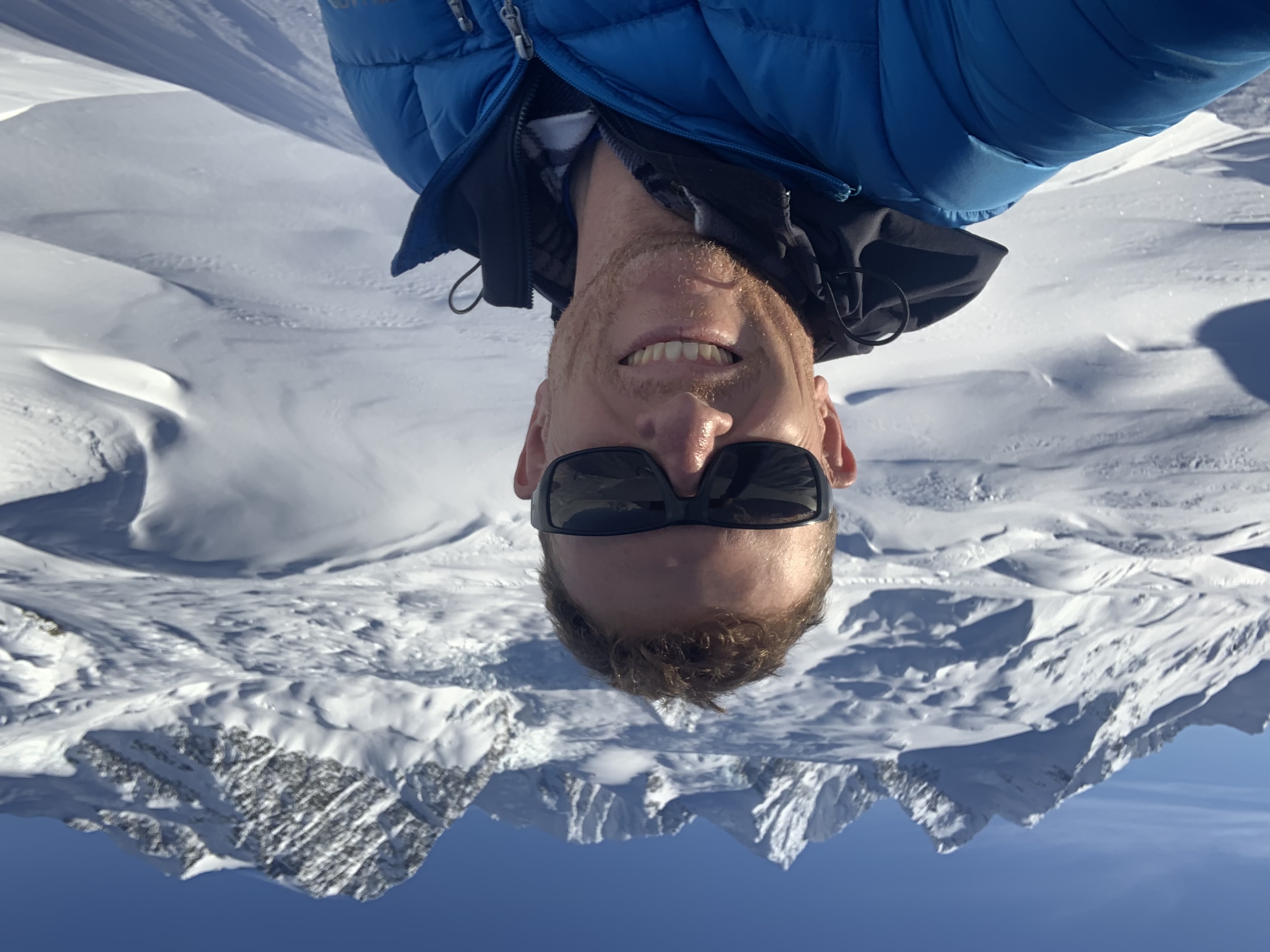 Man with a snowy backdrop smiles at the camera