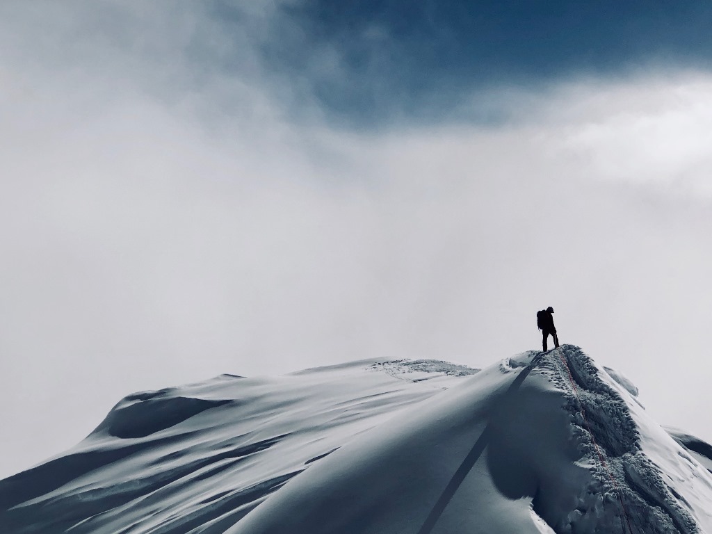 Ranger stands on steep summit ridge looking off into the distance