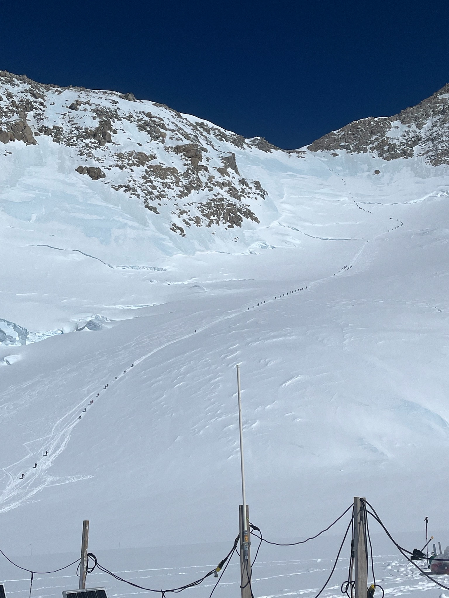 Distant view of a trail of tiny climbers heading up a snowy mountain ridge 