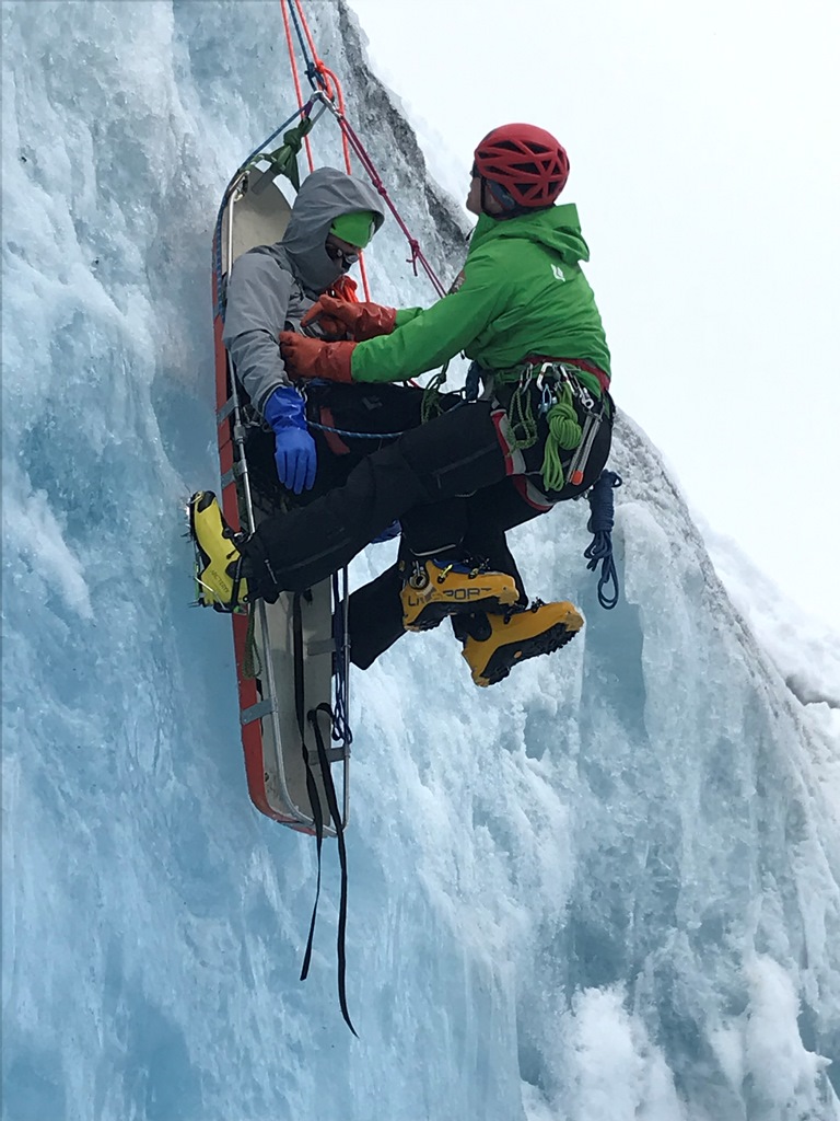 A ranger secures an unresponsive patient to a rescue litter in steep, icy terrain