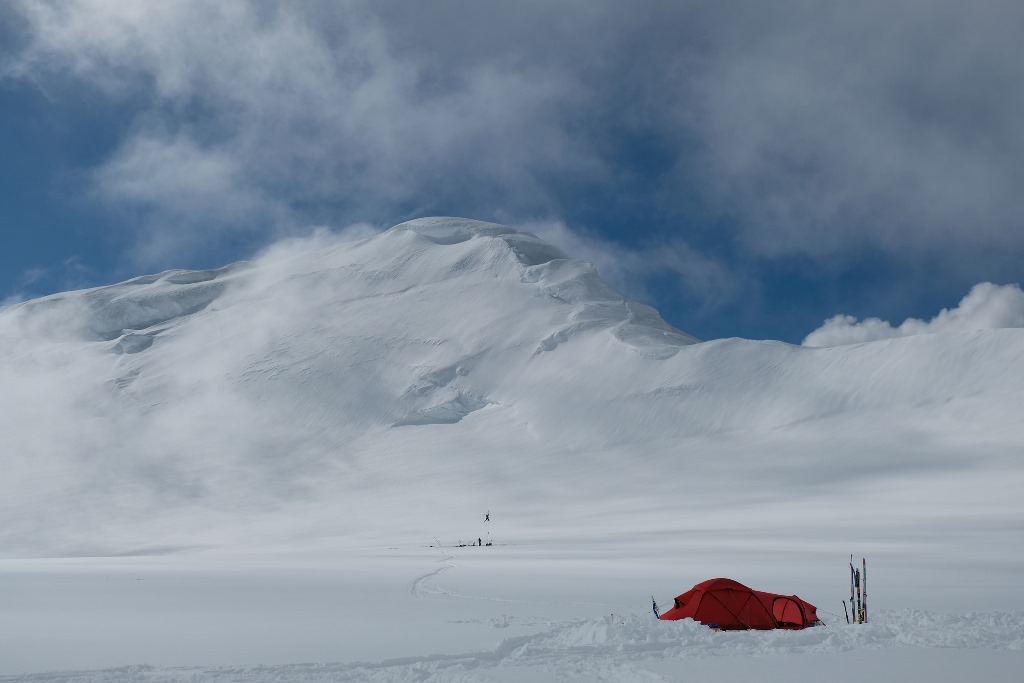 A lone tent in the foreground, Mount Capps in the background. NPS installing a weather antenna in the midground.