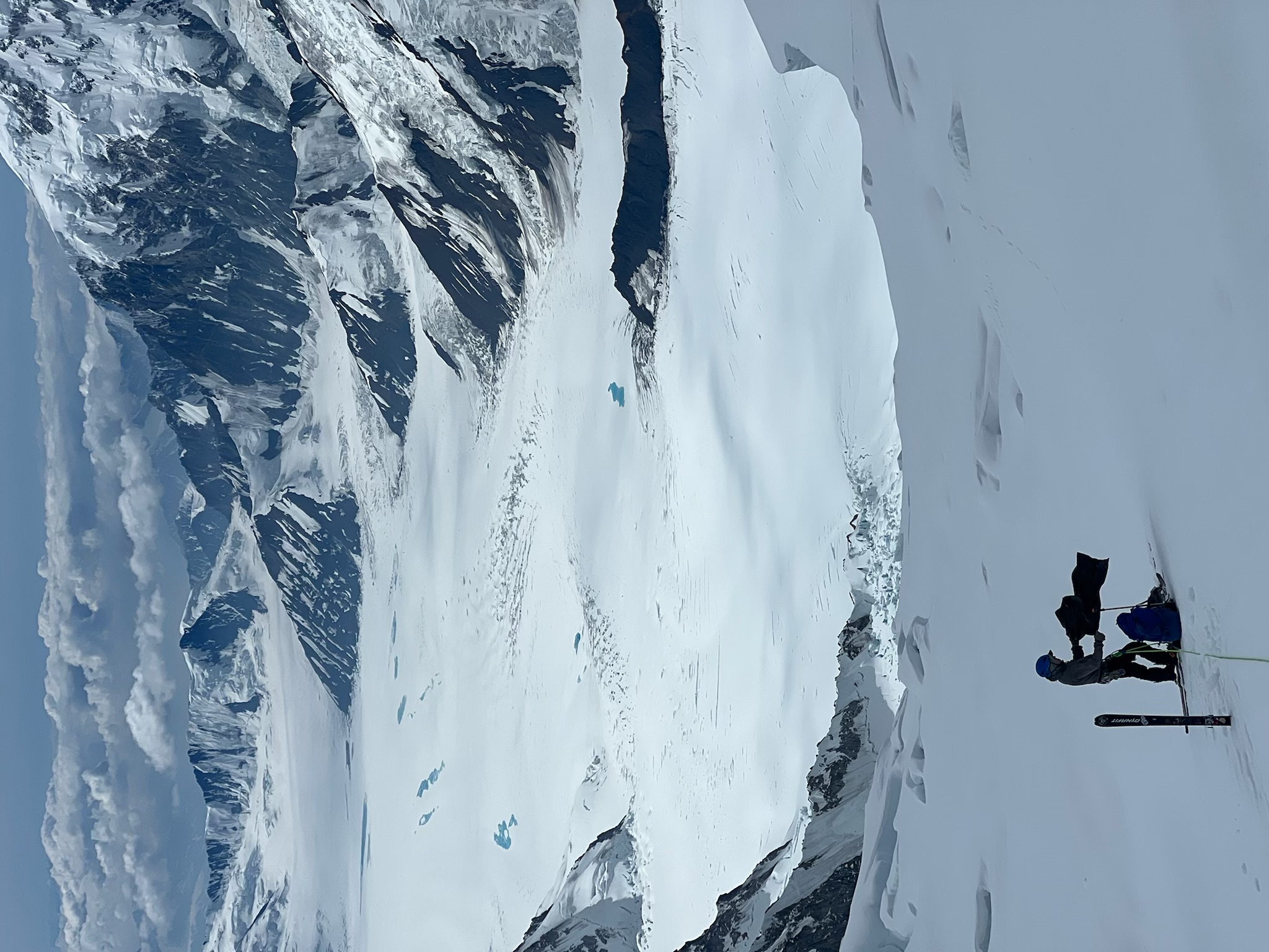 A climber bags some trash on a glacier with a sweeping view of the Alaska Range in the distance