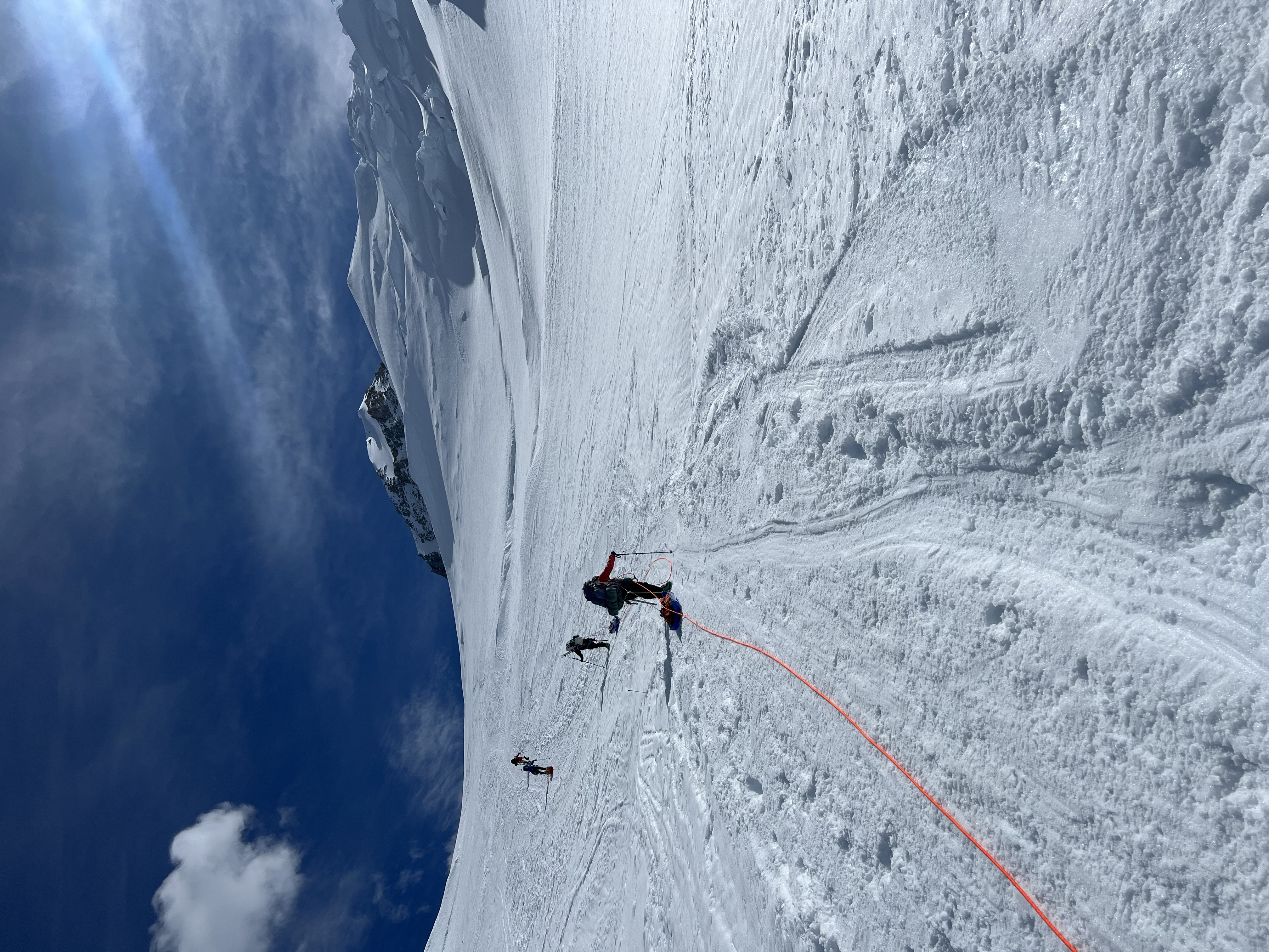 View facing up a glacier at four roped climbers in the distance