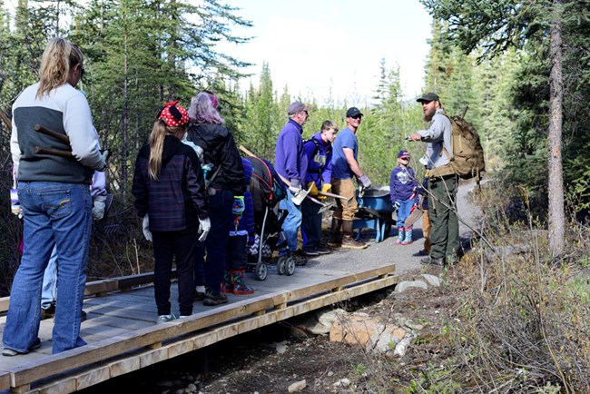 people standing on backcountry trail bridge facing park ranger