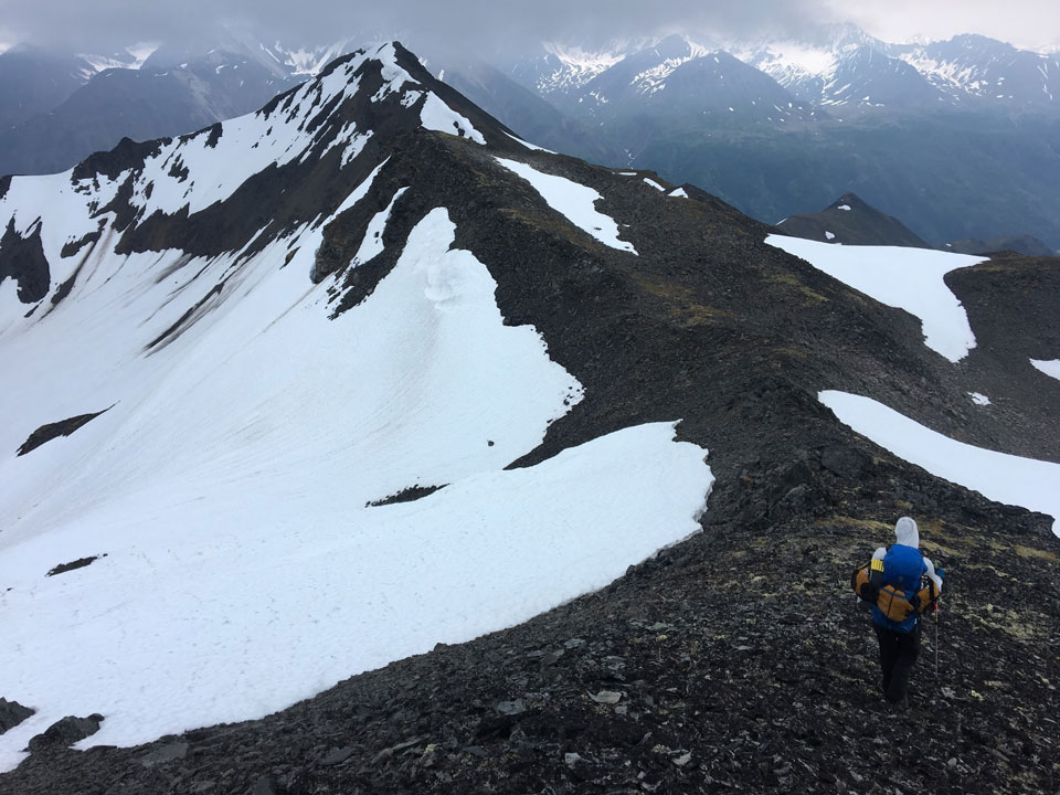 man hiking down a knife-edge ridge on a mountain