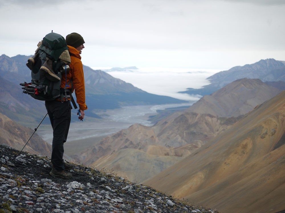 a man standing on a mountaintop looking down at a river far below