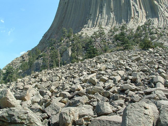 Hundreds of large rocks collected at the base of a giant rock monolith.