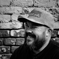 Smiling man with hat in front of brick wall.