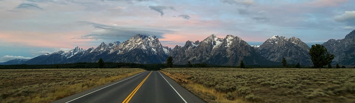 Snow-capped mountains with pink and gray clouds above. A road leads towards the mountains.