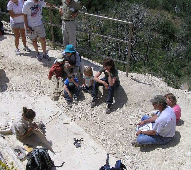 A person sitting on the ground shows a large rock to a group of people