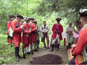 Men in military uniforms circle around freshly disturbed earth