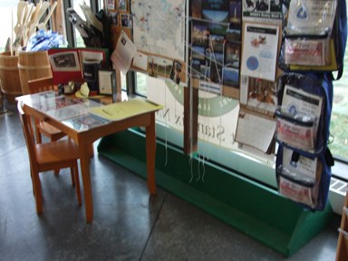 a small golden brown desk with colorful posters and pictures of interesting and beatuful places behind it.