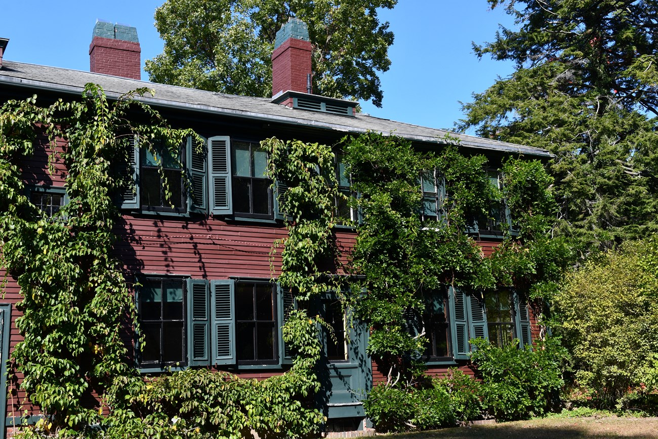 The view of a red home covered in vines from a large green lawn