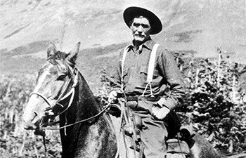 historic image of man wearing hat and suspenders astride horse