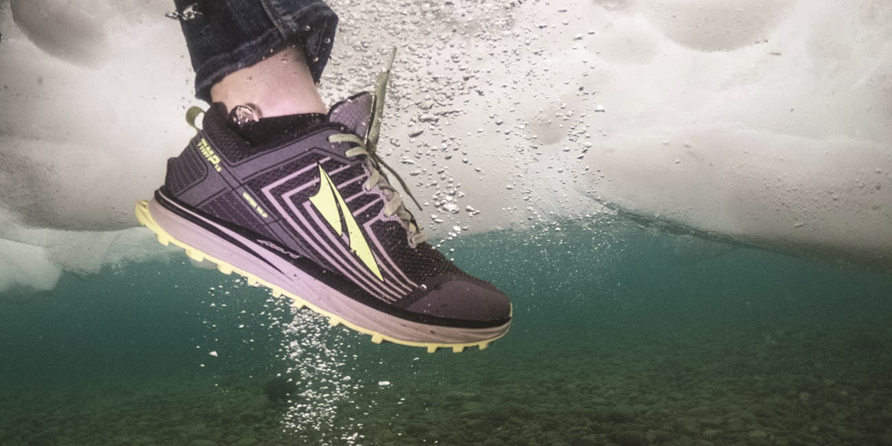 A person's foot sticks down through ice. Green blue water in the background the image is taken from underwater.