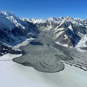 a plume of rock strewn across a snowy basin beneath steep surrounding mountains.