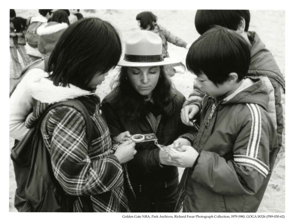 A ranger looks at a magnifying class with two children.