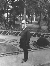 man with bushy beard standing in front of formal gardens