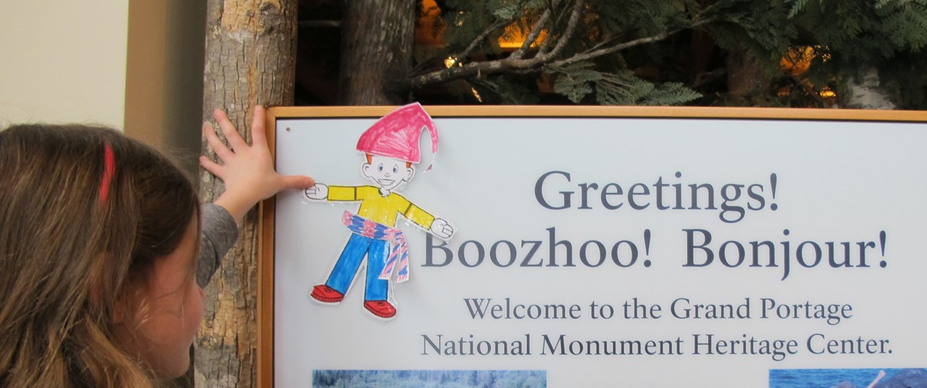 A child holding up a paper voyageur drawing on the welcome board.