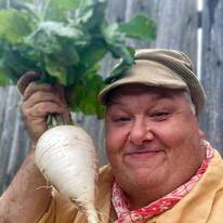 A person in historic clothing holding a large white root with green leaves.