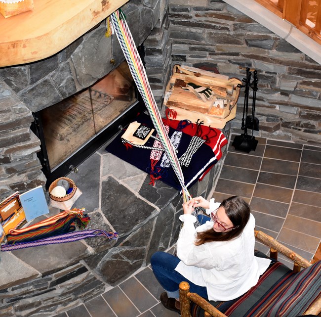 Overhead view of a person finger weaving a colorful arrowhead pattern sash.