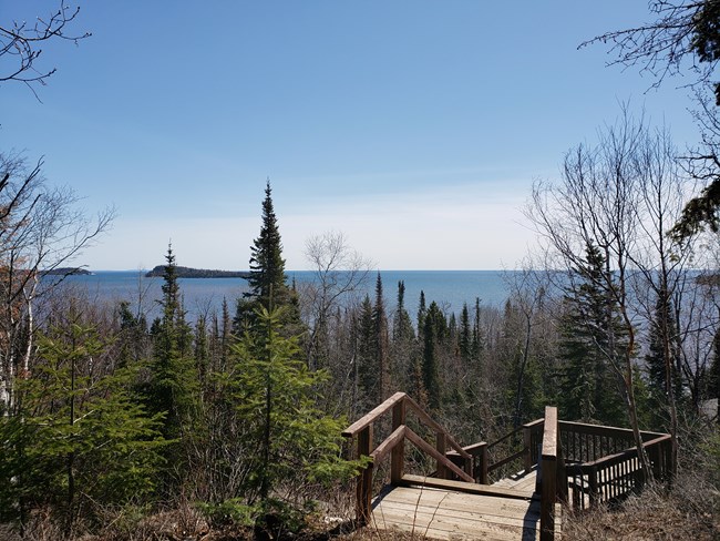 A bay with an island viewed through trees from a wooden staircase.