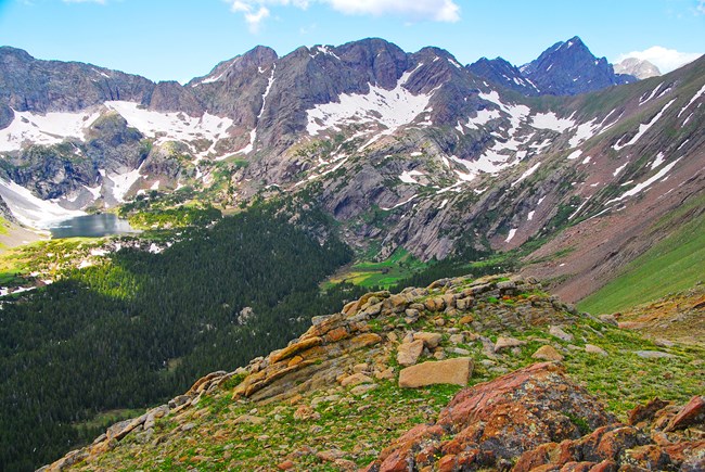 A large alpine mountain basin with snowcapped mountains, lakes, and forests
