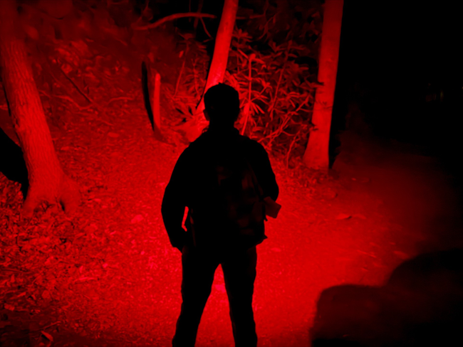 A hikers silouette that appears black in the night hiking on a trail with a red headlamp.