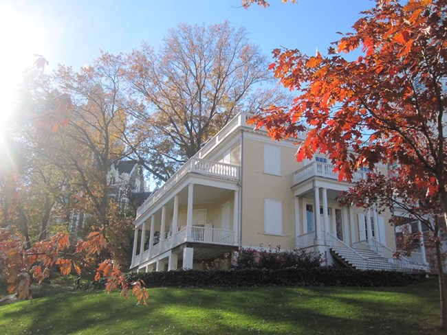 A yellow house stands on a hill surrounded by autumn colored leaves of red.