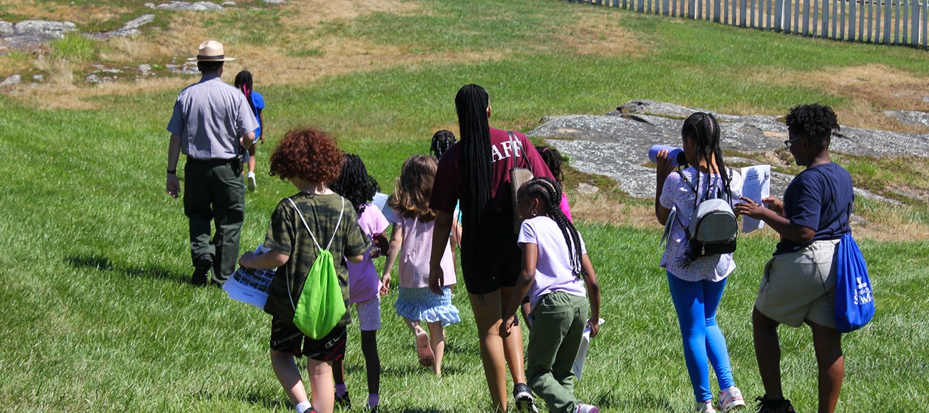 A group of young people running towards the overseer's house. They are following a park ranger.