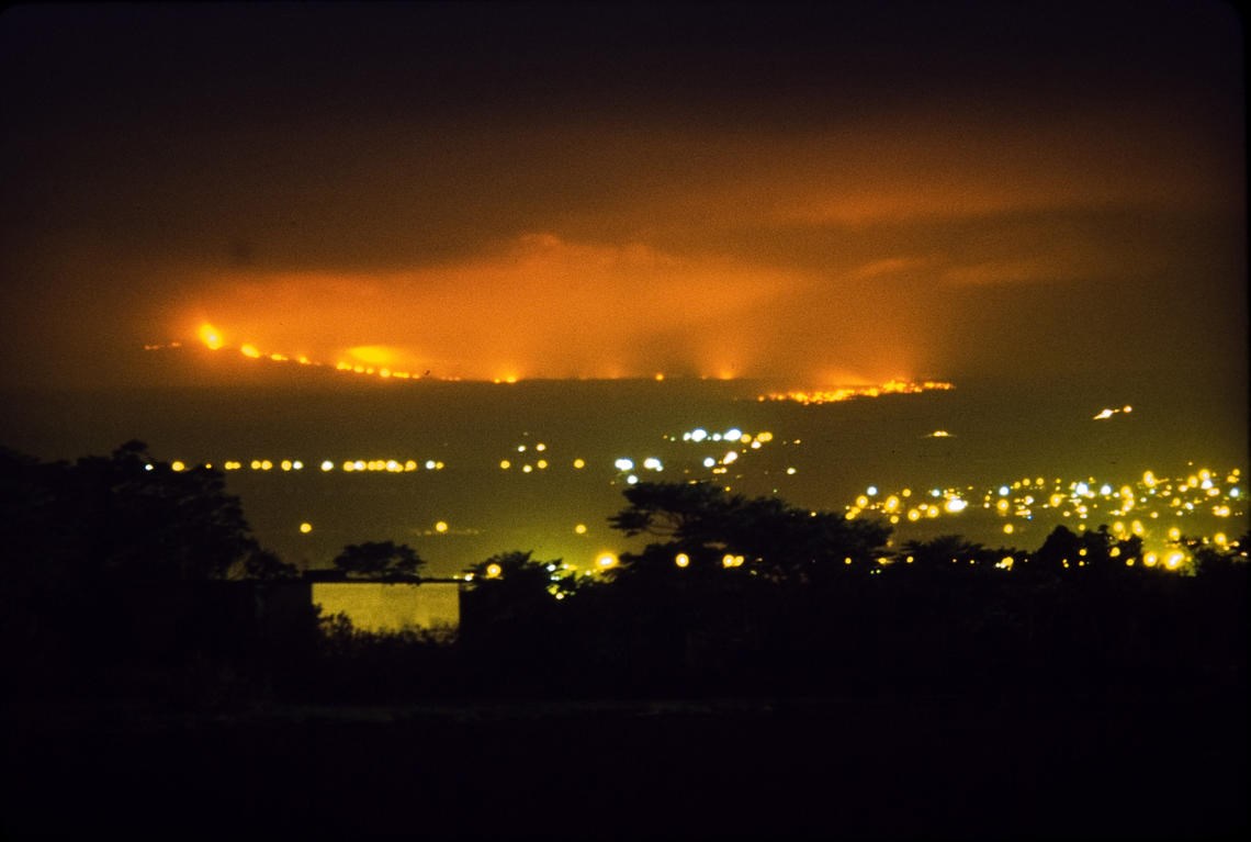 Glowing lava flow descending to city at night