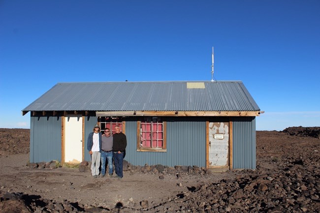 Three men standing in front of a small cabin