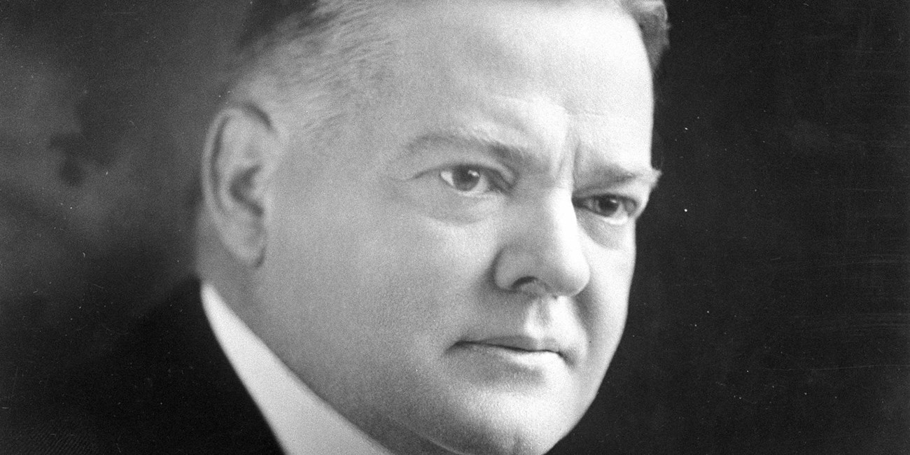 A middle aged man in a suit, tie, and high-collar shirt sits for a portrait photo.